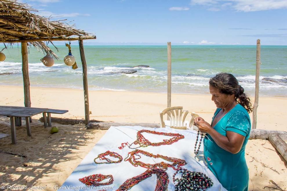 Imagem de artesã fazendo seus colares de sementes na Praia de Caraiva.